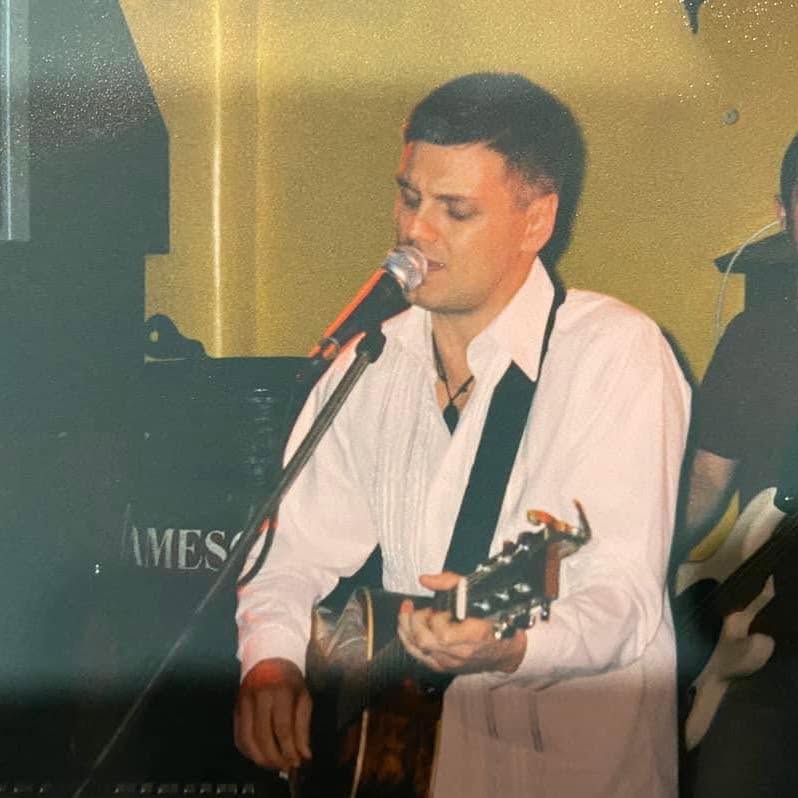 A younger Ryan Edwards in a white shirt singing at a microphone during his London years
