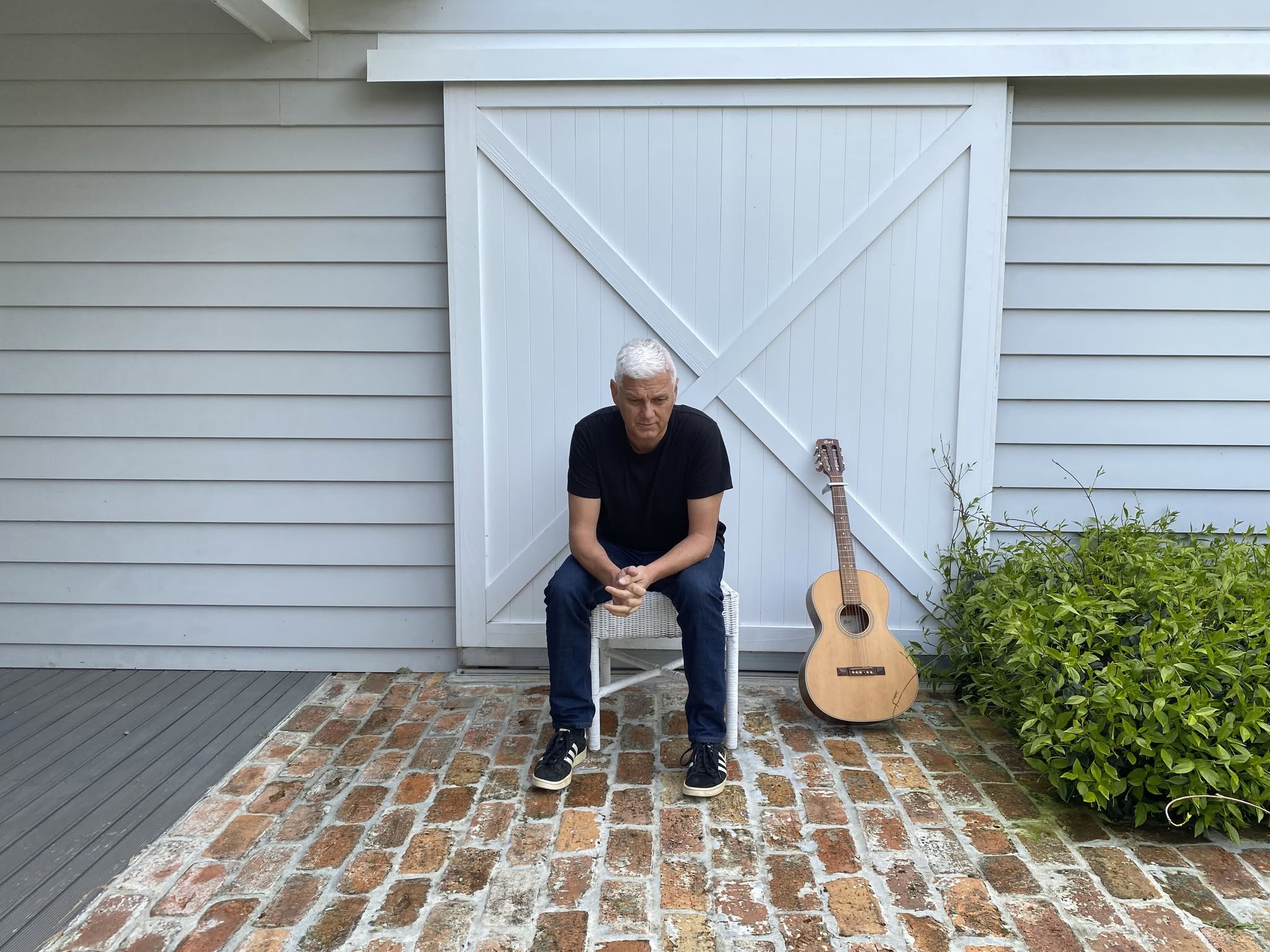 Ryan Edwards seated by a white barn door with a guitar leaning beside him